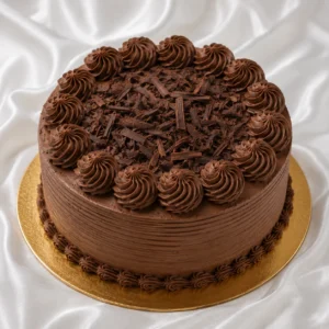 Round chocolate cake with smooth
  chocolate frosting, cream swirls and chocolate shavings on a gold cake board